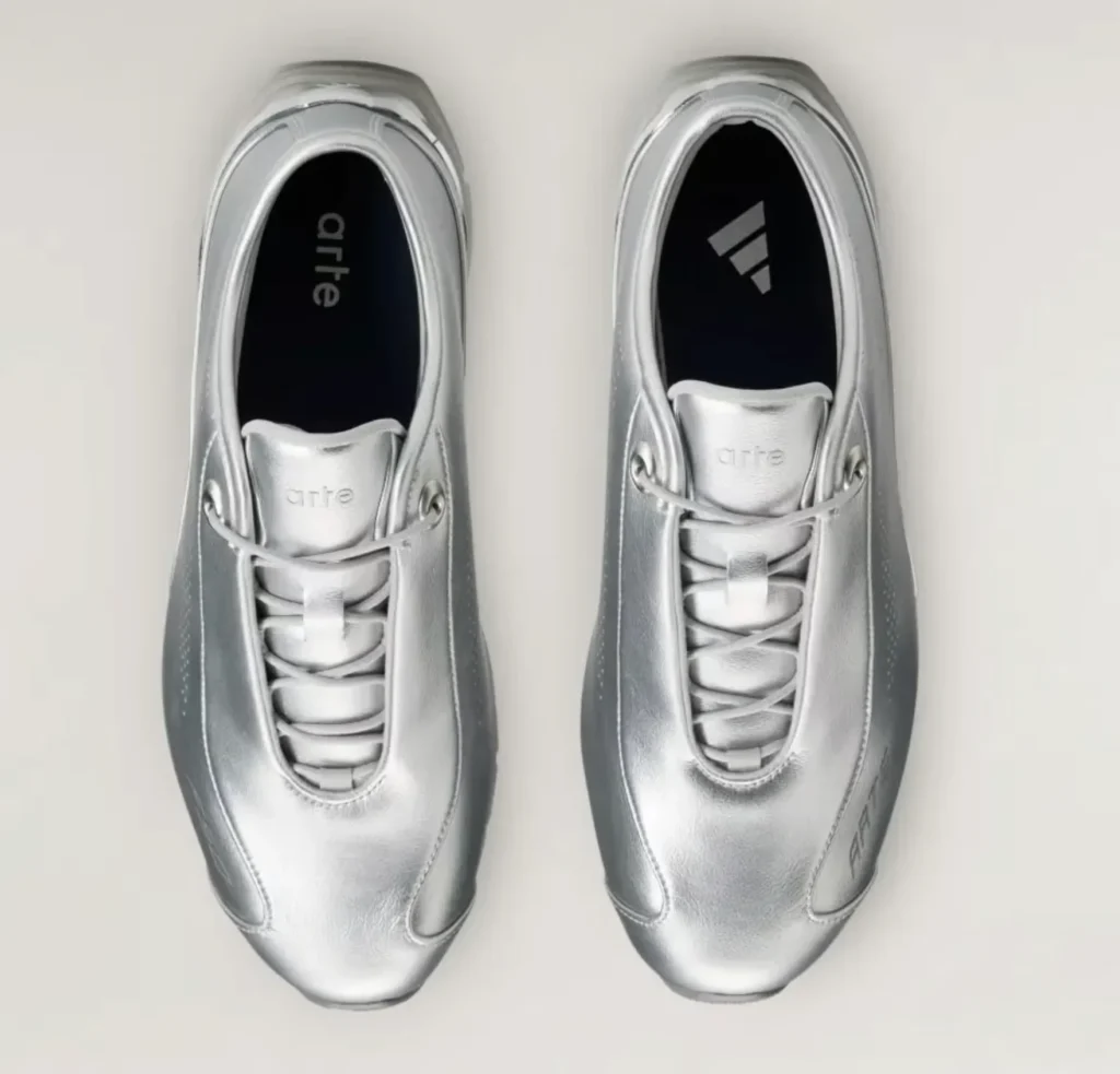 Top-down view of paired metallic silver sneakers with white laces, black insoles, and Arte and adidas logos on a white