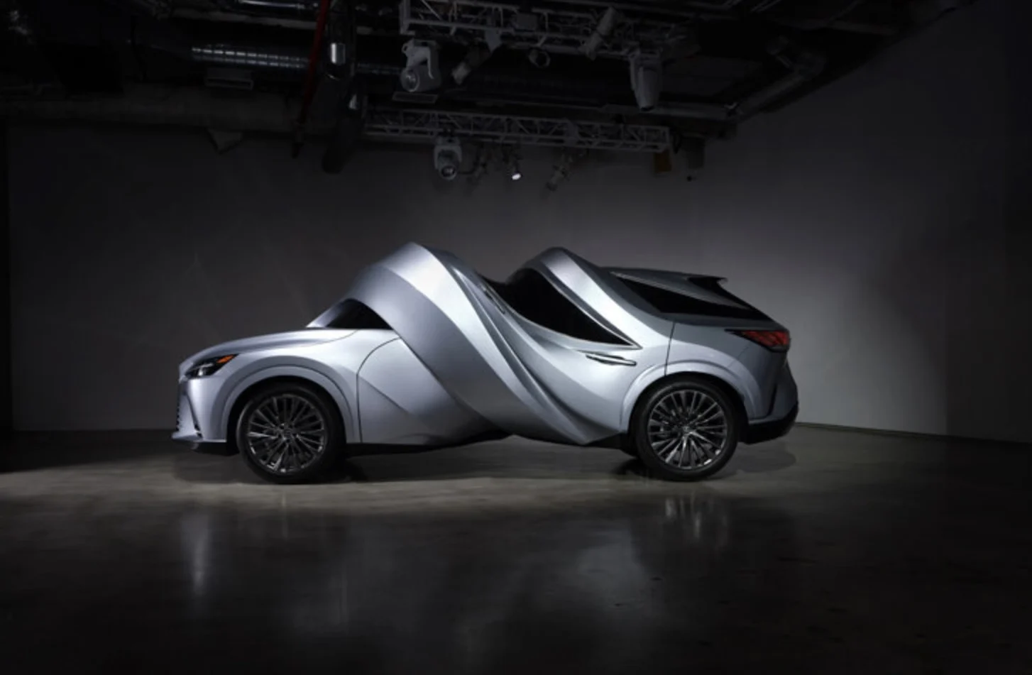 Silver Lexus EV sculpture with its body twisted into a dramatic mid-swerve shape in a dark gallery gallery