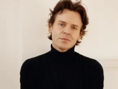 Christopher Kane poses facing the camera in a black turtleneck against a plain cream wall