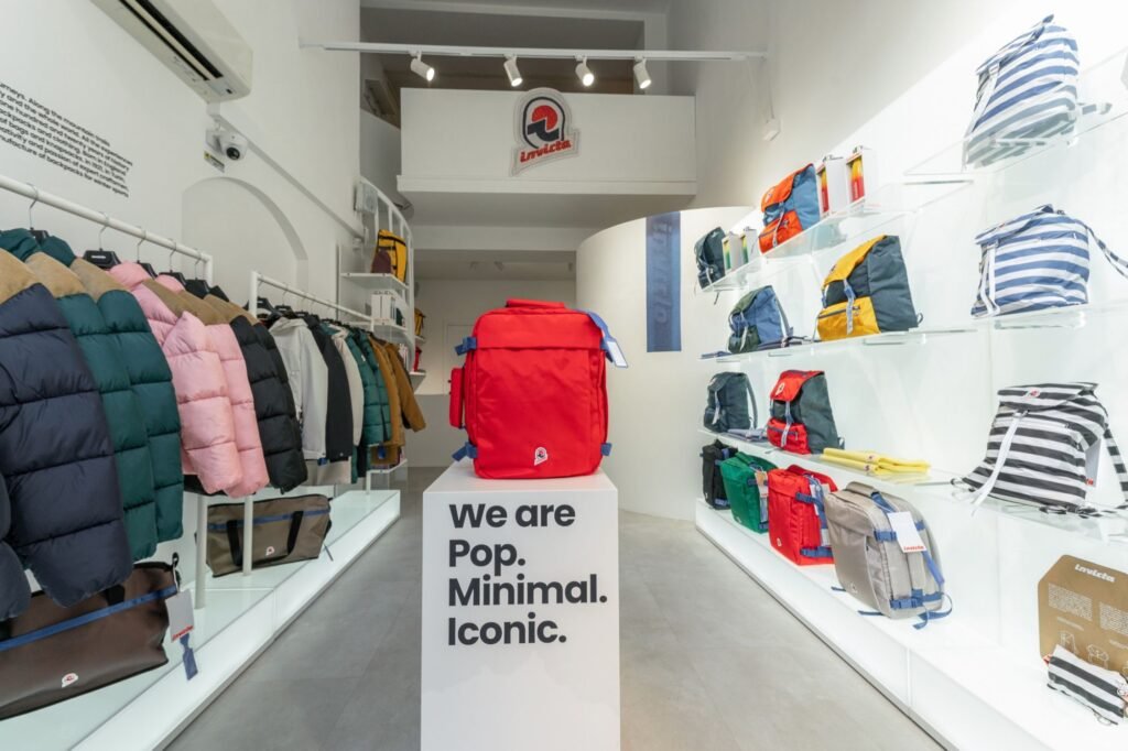 Invicta store interior with colorful puffer jackets and backpacks, centered on a bright red backpack atop a branded pedestal