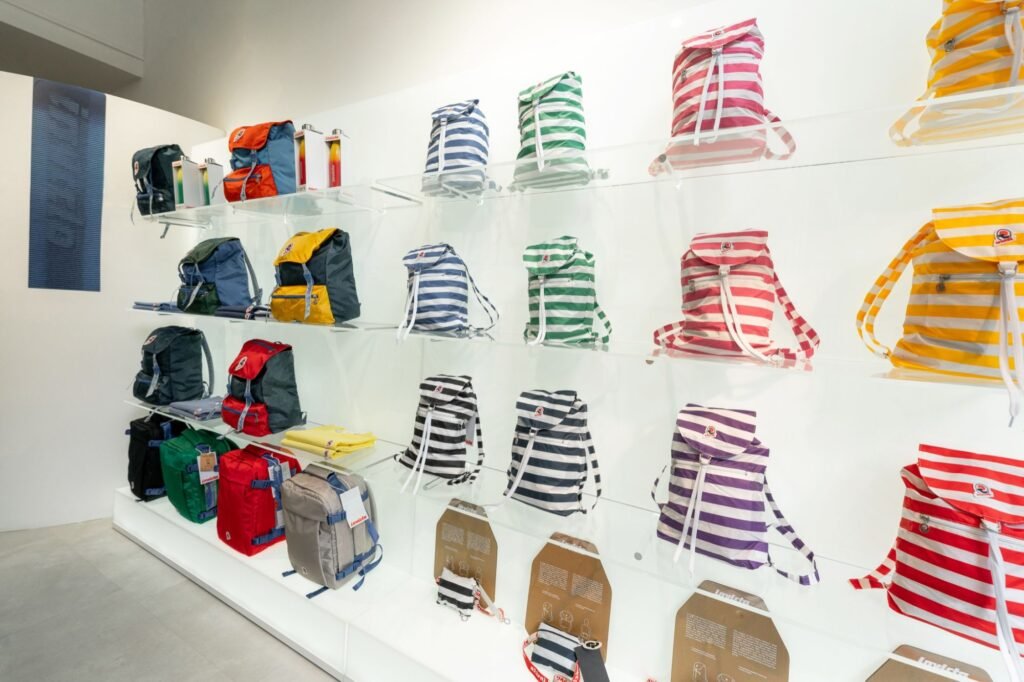 Invicta backpacks in solid and multicolored striped designs displayed on white glass shelves in a store alcove