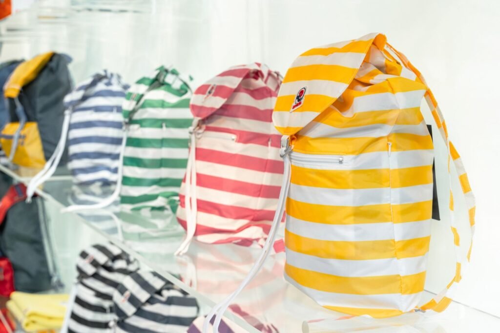 Striped Invicta backpacks in yellow, pink, green, blue, and black displayed on glass shelves