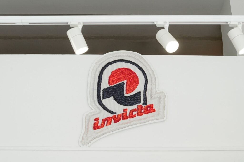 Embroidered Invicta logo mounted on a white wall beneath ceiling track lights