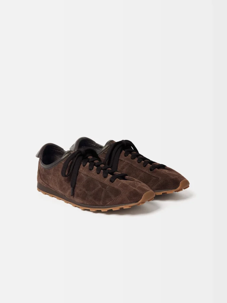 Pair of low-profile brown suede sneakers with black laces and gum rubber soles on a white background