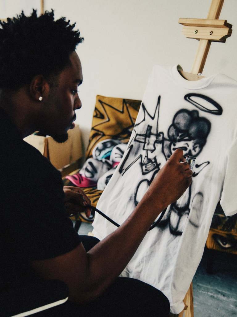 Person spray-paints a cartoon-style design onto a white T-shirt stretched on an easel