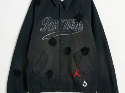 Black Jordan jacket with floral appliqués, gray NÒMARHYTHM lettering, red Jumpman logo and white emblem on white background