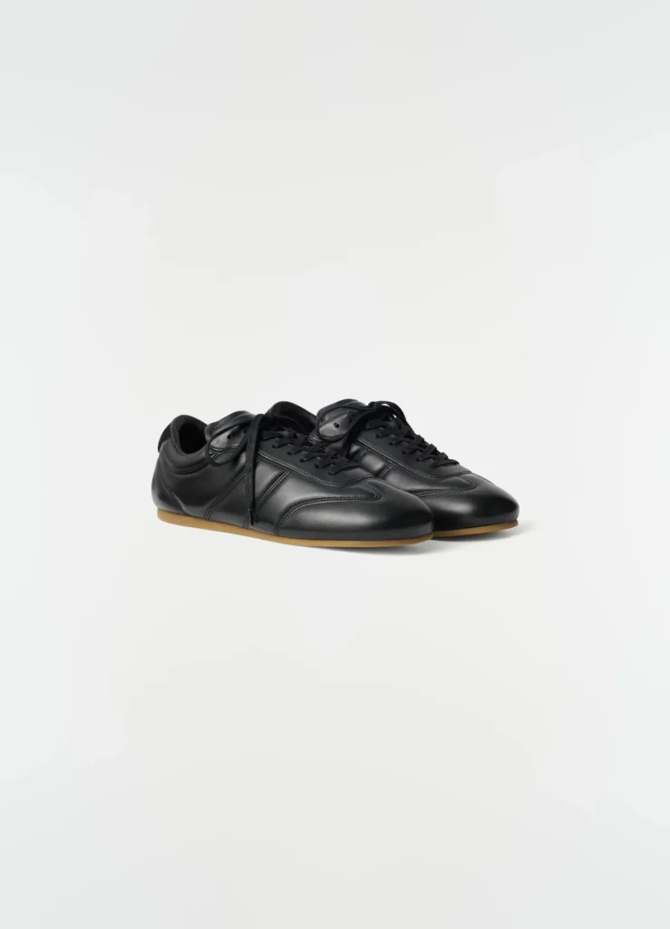 Pair of black leather low-profile sneakers with black laces and gum-colored soles on a white background
