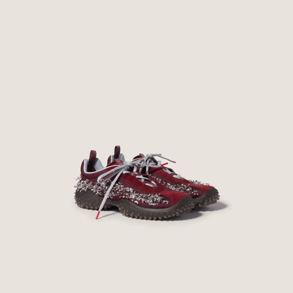 Pair of burgundy sneakers with gray laces, crystal embellishments, and low lugged soles on a pale background