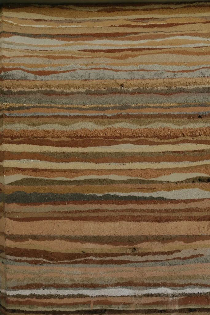 Close-up of a wall with horizontal, uneven layers of earthy tan, red, gray, and white material