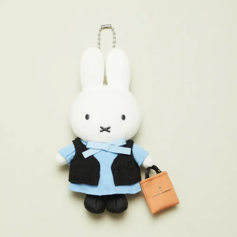White rabbit plush keychain wearing a blue dress and black vest, holding an orange United Arrows bag against a pale
