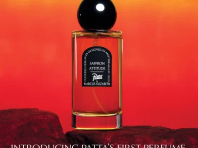 Perfume bottle with black spherical cap and amber liquid on dark rocks against a yellow-to-red gradient background