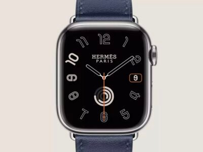 Hermès Apple Watch with navy leather band, silver case, and black dial with outlined numerals on a beige background