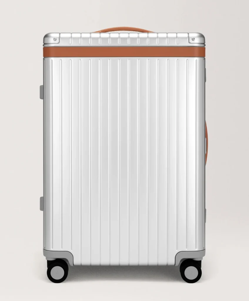 White ridged hard-shell suitcase with brown trim and handle, shown front-facing on four wheels against a pale background