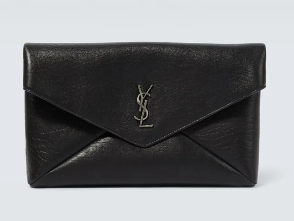 Black leather Saint Laurent envelope clutch with a pointed flap and silver YSL logo, centered on a pale background