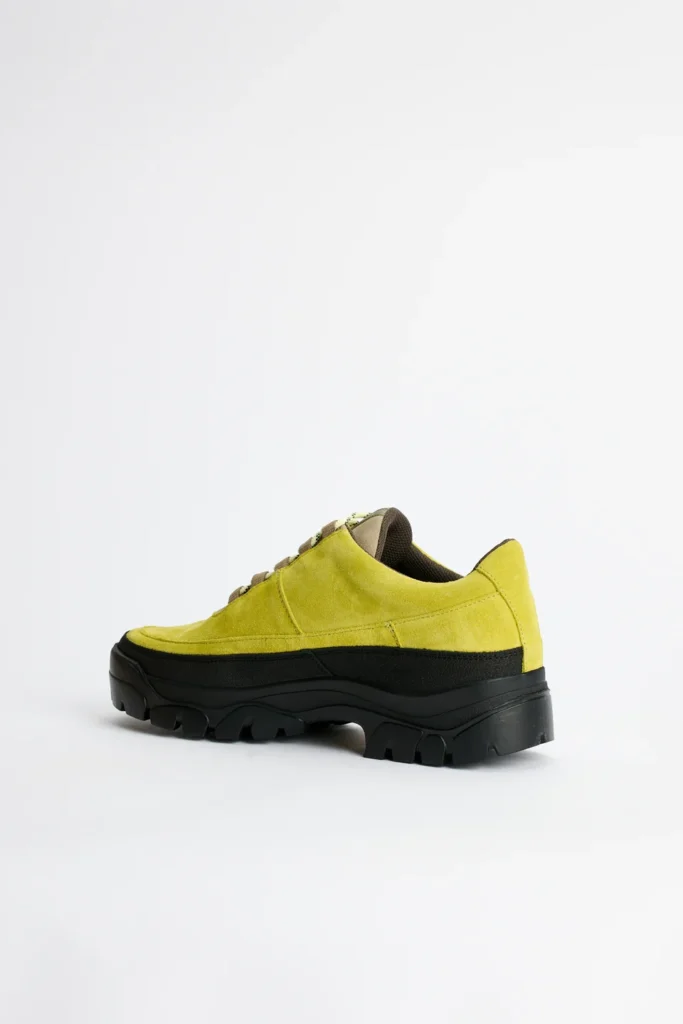 Lime green suede low-top shoe with brown laces and a thick black lugged sole on a white background