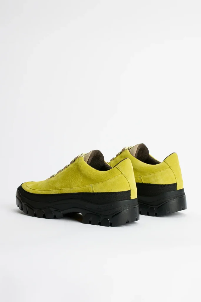 Pair of lime-green suede shoes with black panels and chunky lugged soles on a white background