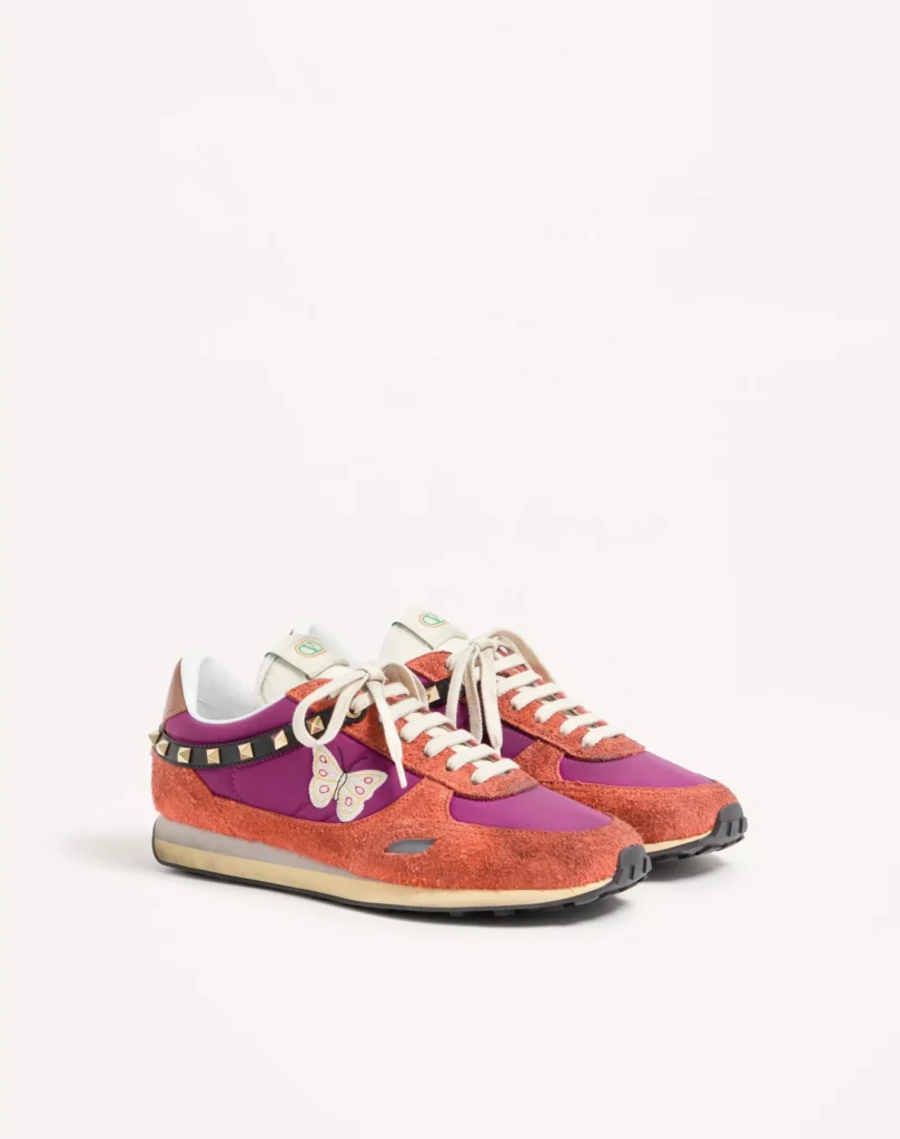 Pair of low-top Valentino sneakers in coral suede and purple fabric, with cream laces, studs, and a butterfly detail