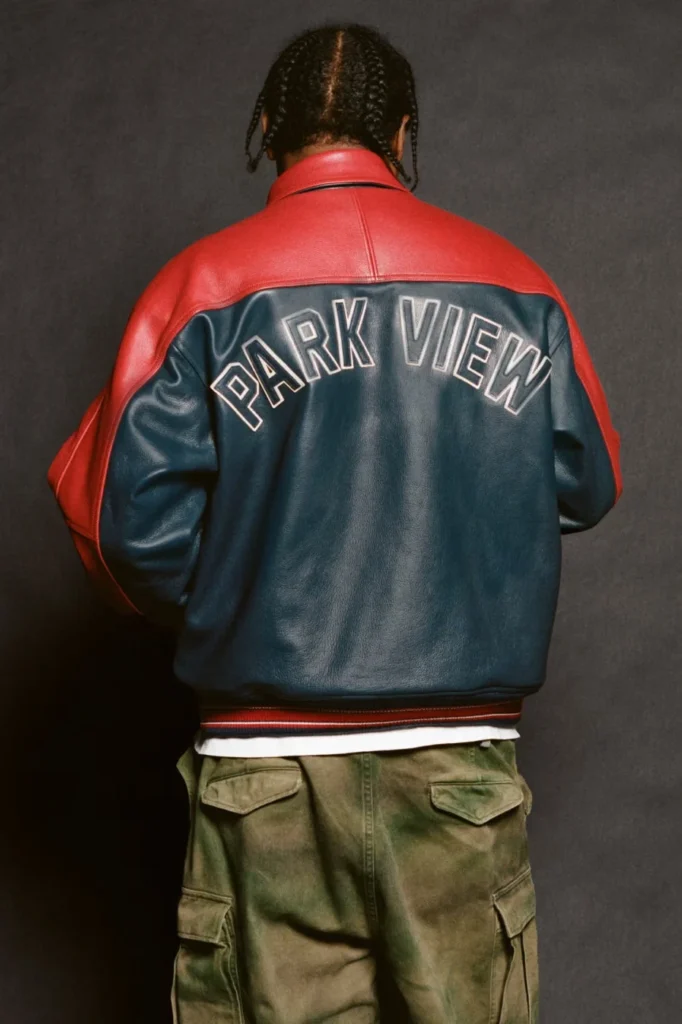 Person seen from behind wearing a red and navy leather jacket labeled “PARK VIEW” and olive cargo pants against a dark
