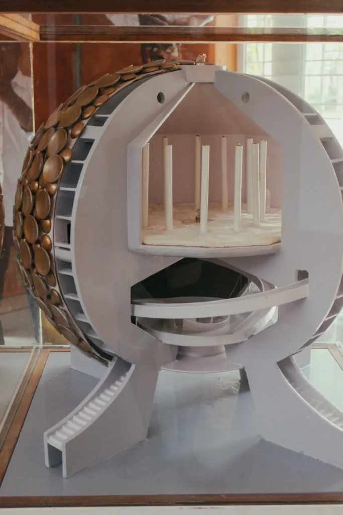 White spherical architectural model with bronze discs, open tiers, and slender interior columns displayed indoors behind