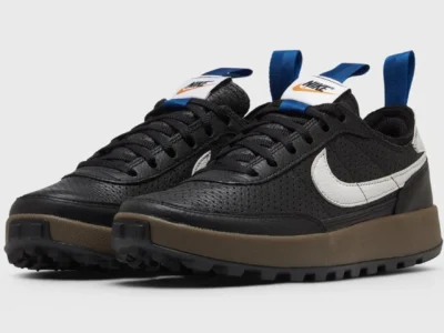 Pair of black Nike sneakers with white Swooshes, blue pull tabs, brown midsoles and rugged black outsoles on white background
