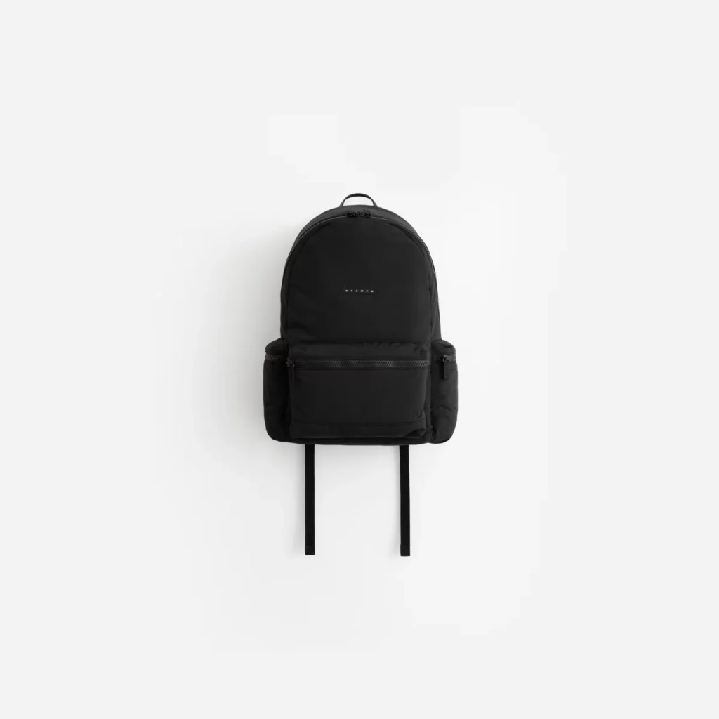 Black backpack with multiple zippered compartments, a small logo patch, and hanging shoulder straps on a white background