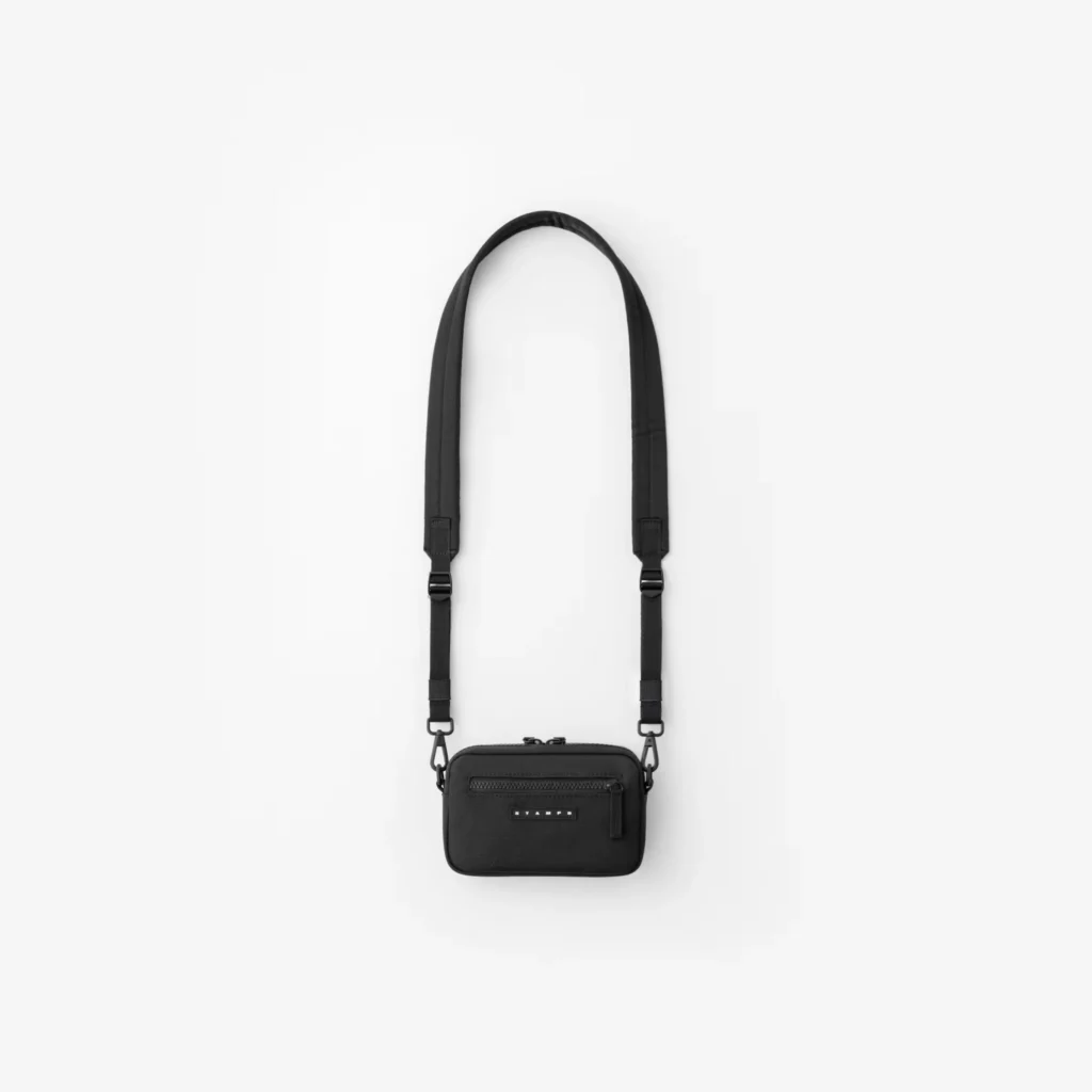 Black rectangular crossbody bag with adjustable strap, front zip pocket and small Stampd label on a white background