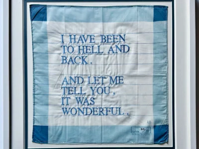 Framed blue-and-white textile artwork with embroidered text, “I HAVE BEEN TO HELL AND BACK. AND LET ME TELL YOU, IT WAS