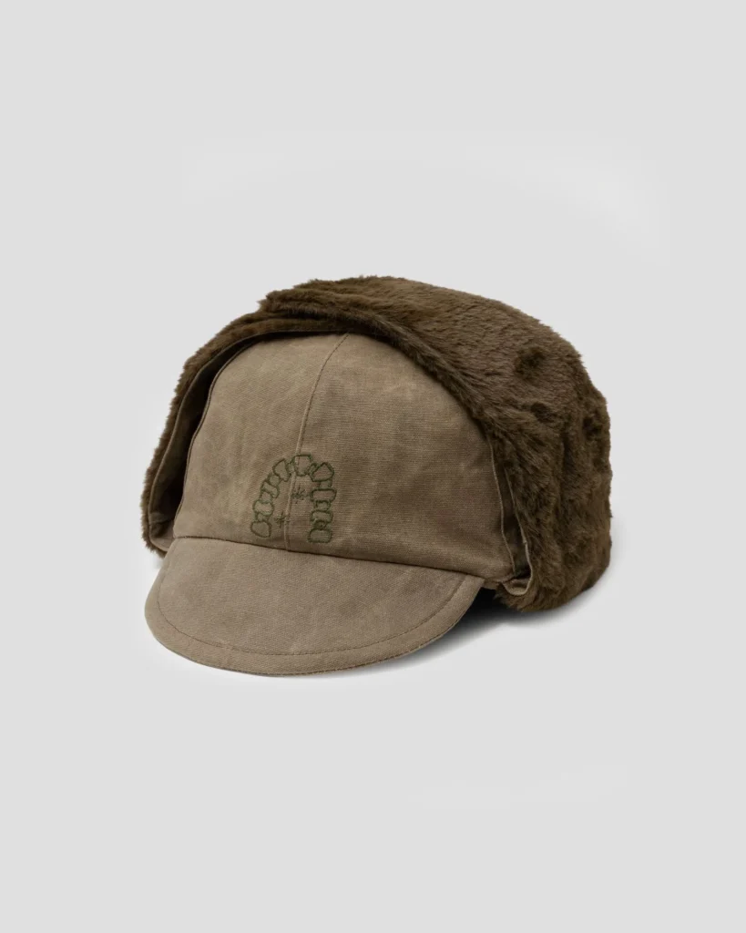 Brown canvas cap with a curved brim and dark brown faux-fur ear flaps, shown against a light gray background