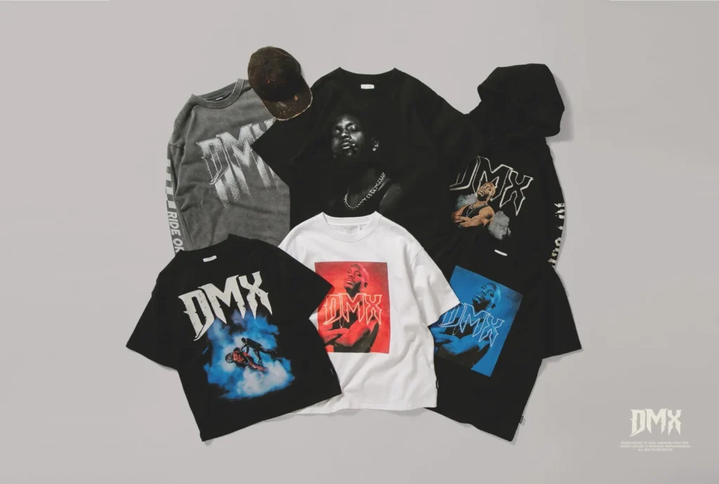 Flat lay of DMX graphic T-shirts in black, gray, and white, plus a dark cap, arranged on a light background