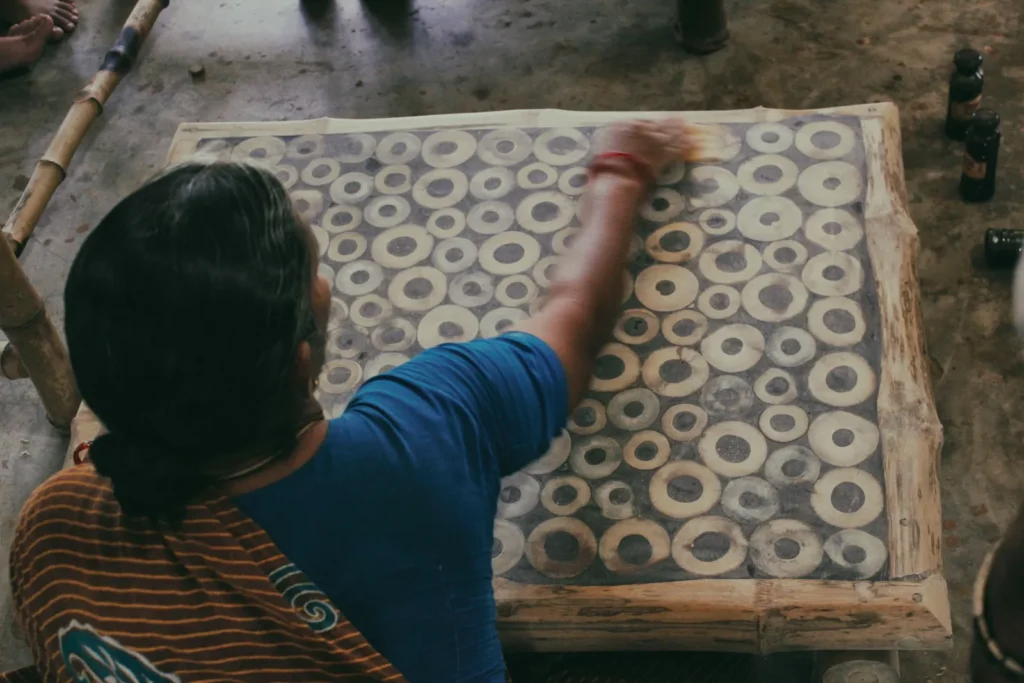 Person in blue shirt applies material to a wooden panel covered with cream and gray circular patterns in a workshop