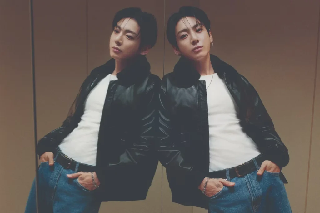 Jung Kook poses with hands in his jeans pockets beside his reflection, wearing a black leather jacket and white shirt in an