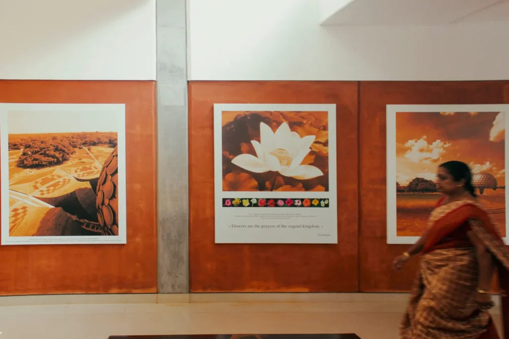 Woman in a patterned sari walks past framed orange-toned photographs and a lotus print on a wood-paneled gallery wall