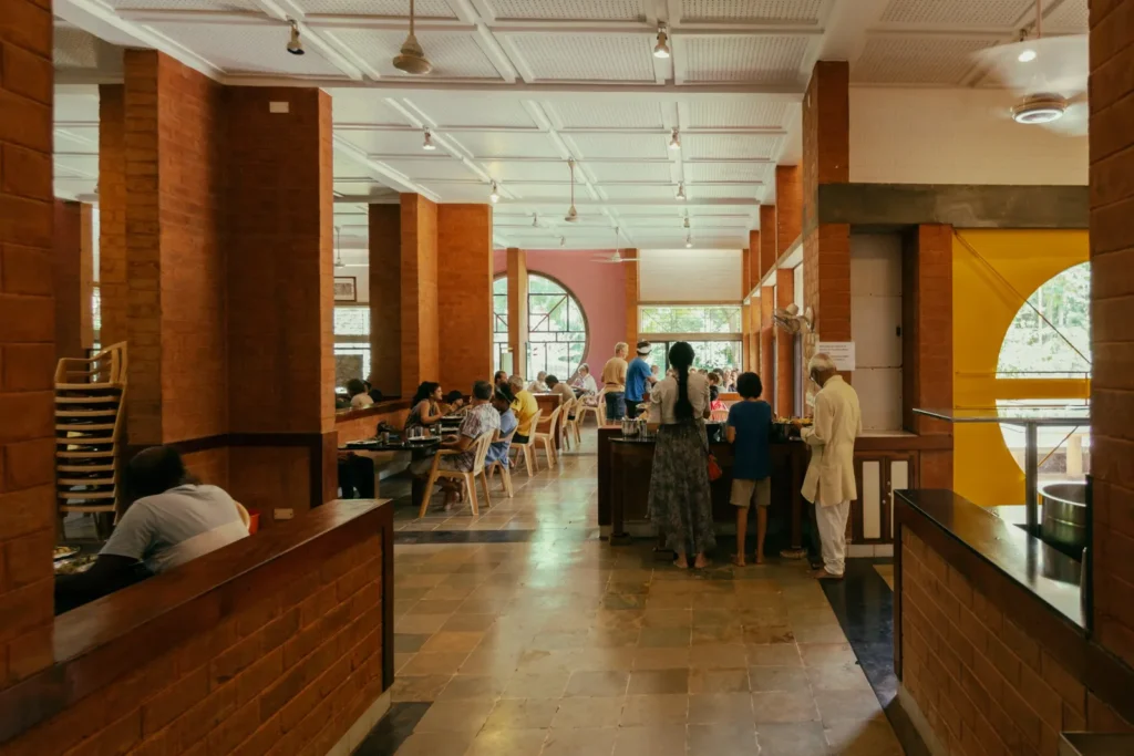 People dine inside a brick-walled cafeteria with arched windows, tiled floors, and a white paneled ceiling