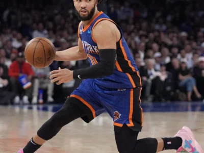 Jalen Brunson dribbles a basketball while lunging across a court in a blue and orange Knicks uniform and pink sneakers