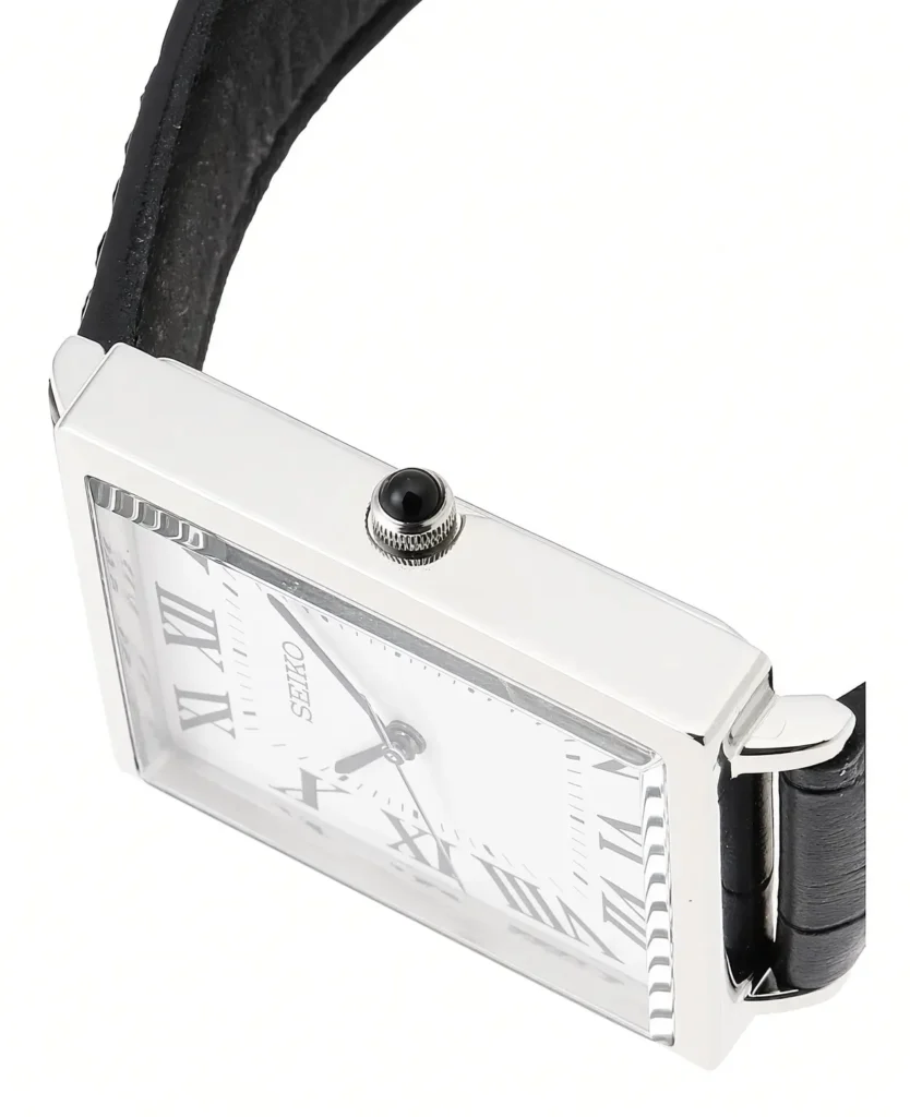 Close-up of a rectangular Seiko watch with a polished steel case, white Roman numeral dial, black crown and leather strap on