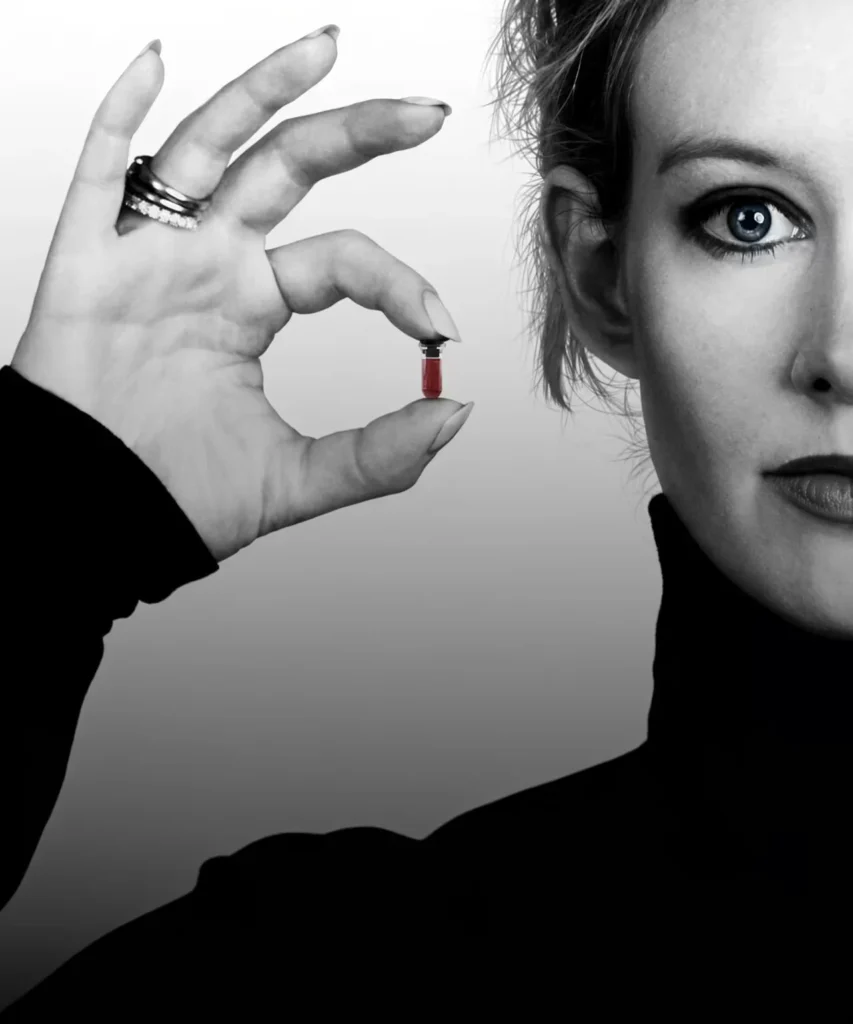 Black-and-white close-up of Elizabeth Holmes holding a red vial beside her face, wearing a black top and rings