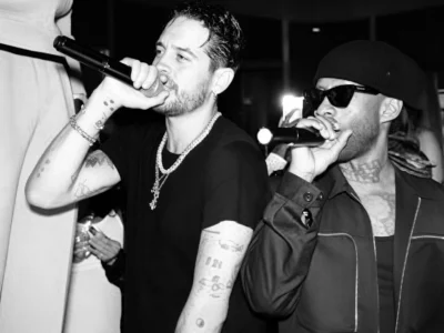 G-Eazy and Ty Dolla $ign perform into microphones, wearing black outfits, jewelry, sunglasses and a beanie in a dim venue