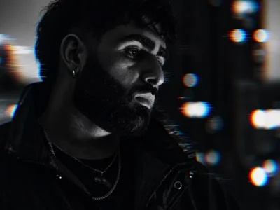 Close-up portrait of fatpapi in a black jacket and hoop earring, surrounded by blurred colored lights