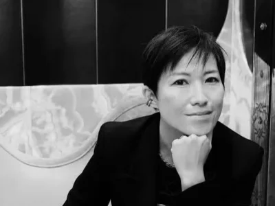 Monochrome portrait of a Sandra Choi in a dark blazer resting her chin on her hand indoors