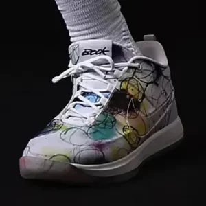 Close-up of a white high-top shoe with colorful abstract scribbles, white laces, and ribbed sock against a black
