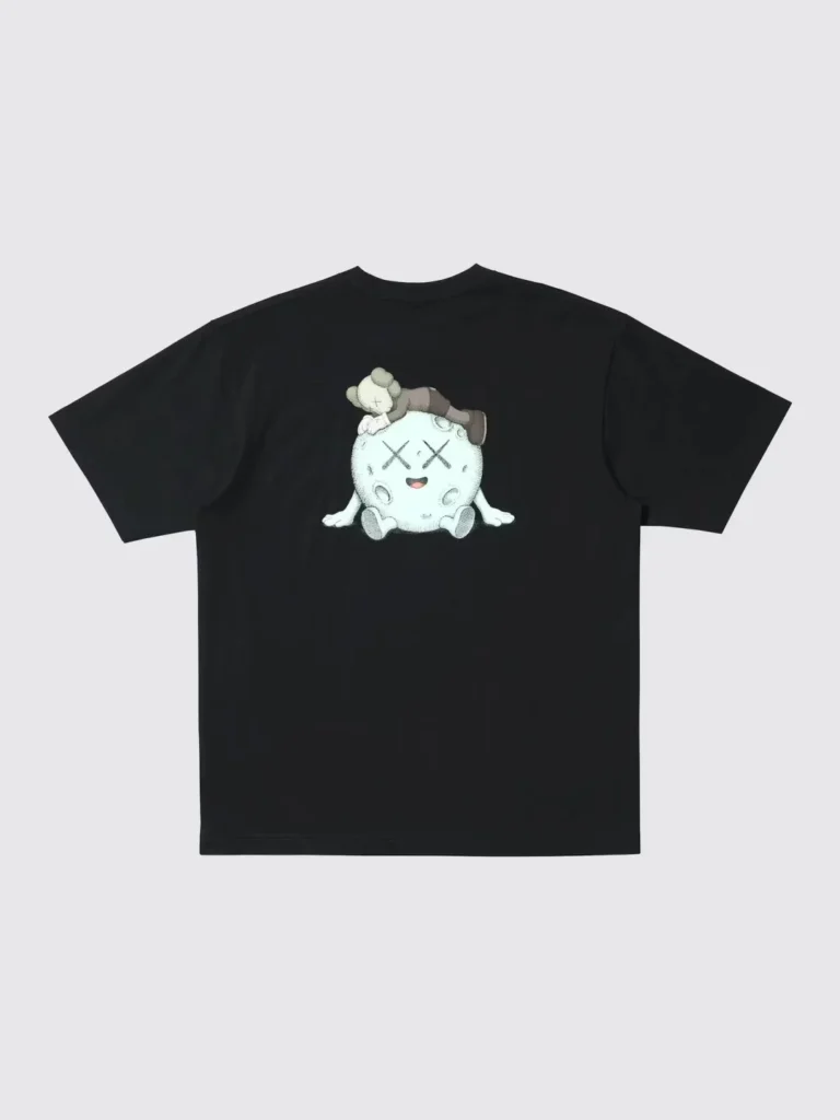 Black Tee with a central white cartoon character graphic featuring crossed-out eyes and a brown figure on its head, laid