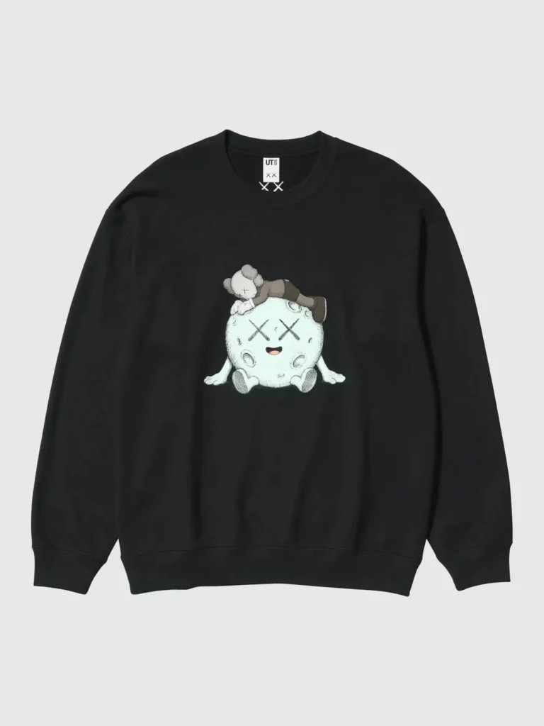Black crewneck sweatshirt with a central graphic of a small figure lying on a round white character, shown against a light