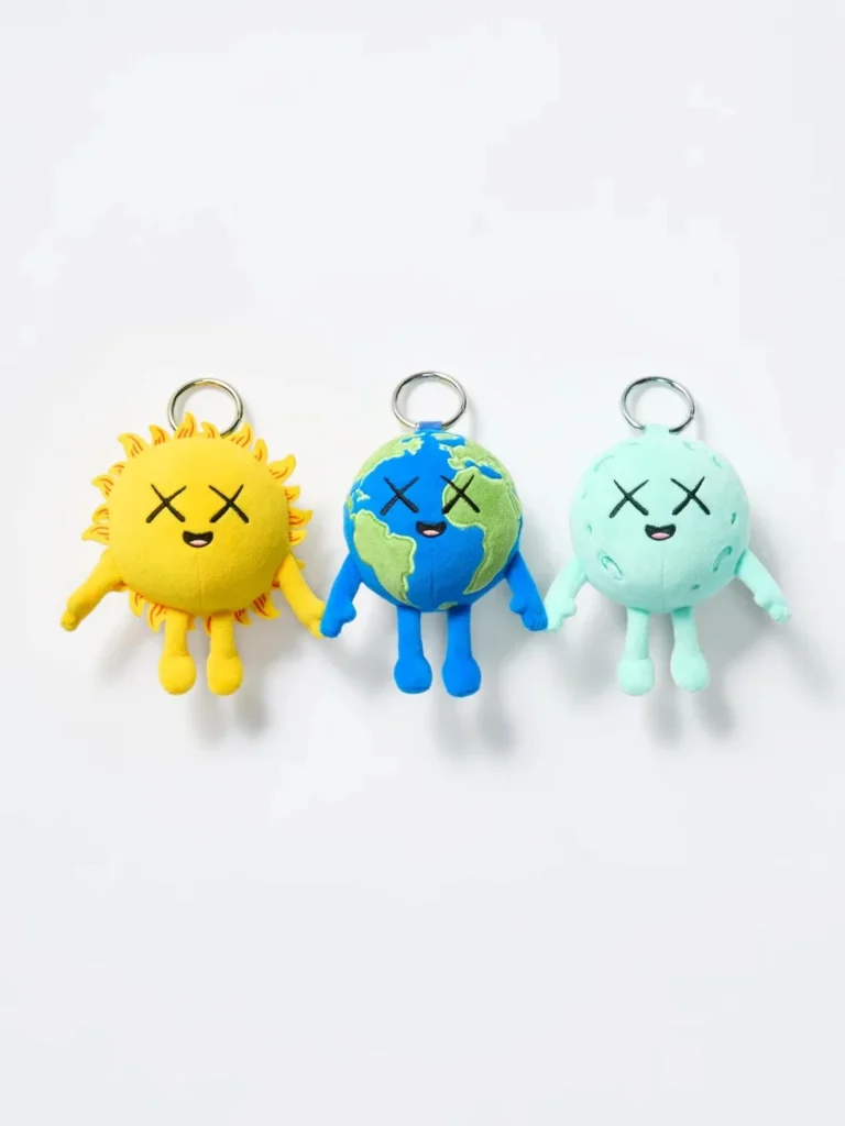 Three plush keychains: a yellow sun, blue-and-green globe, and mint planet, each with crossed eyes and limbs