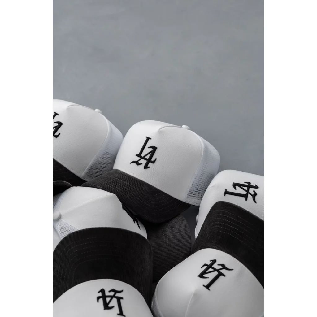 Close-up of overlapping white-and-charcoal mesh trucker caps with black embroidered logos against a gray background