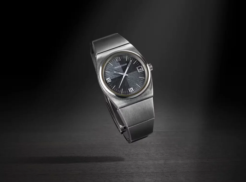 Jaeger-LeCoultre stainless steel watch with dark dial and integrated bracelet, standing on a dark surface against a black