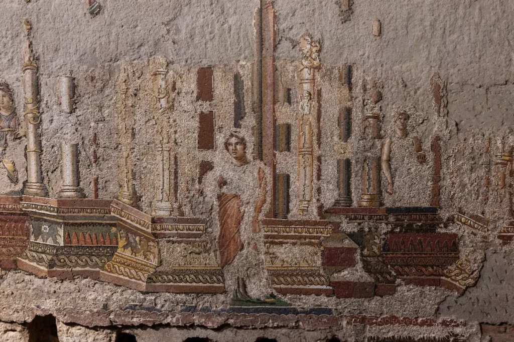 Ancient Roman mosaic fragment showing a seated woman among ornate columns and architectural motifs on a weathered wall