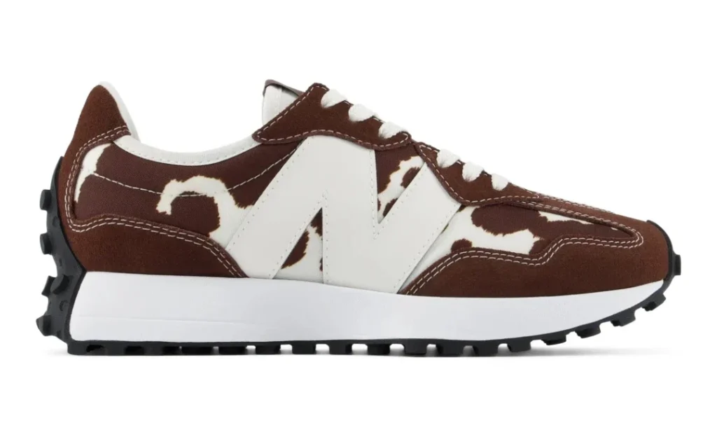 Side view of a brown-and-white New Balance shoe with cow-print panels, white logo, white midsole, and black lugged sole