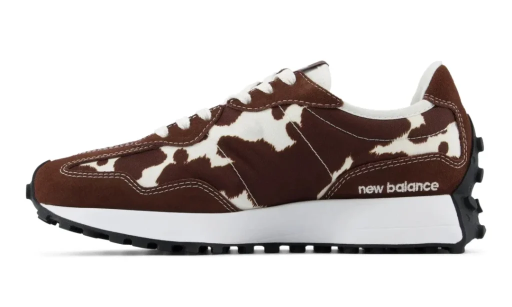 Side view of a brown and white cow-print New Balance shoe with white midsole and black lugged outsole on a white