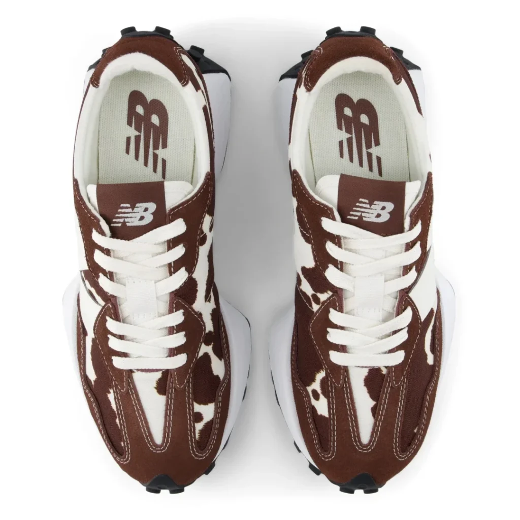 Pair of brown-and-white cow-print New Balance sneakers with white laces, viewed from above on a white background