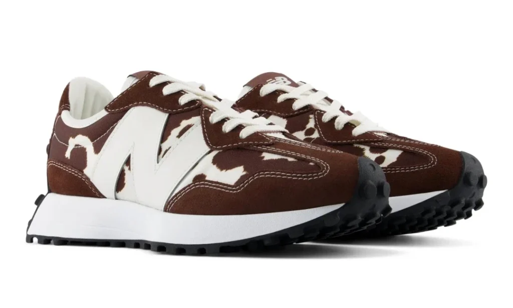 Pair of brown and white cow-print New Balance sneakers with white laces, oversized logos and black lugged soles on white